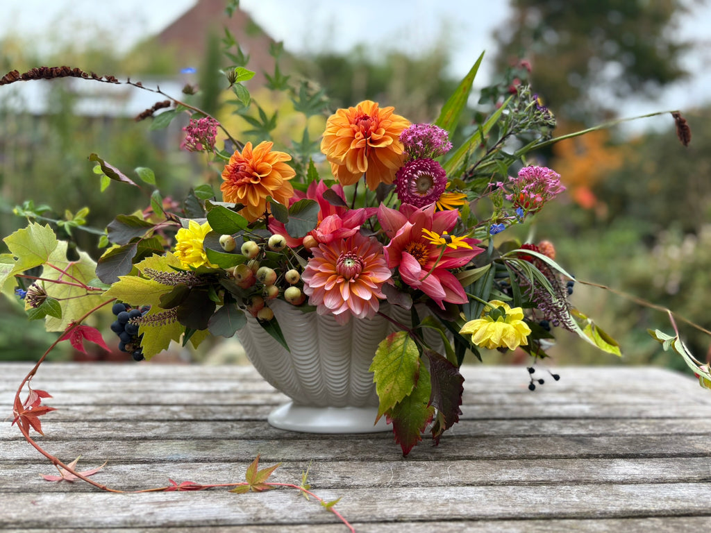 Colorful floral arrangement in a white Dartmouth mantel vase on a wooden table with a blurred garden background