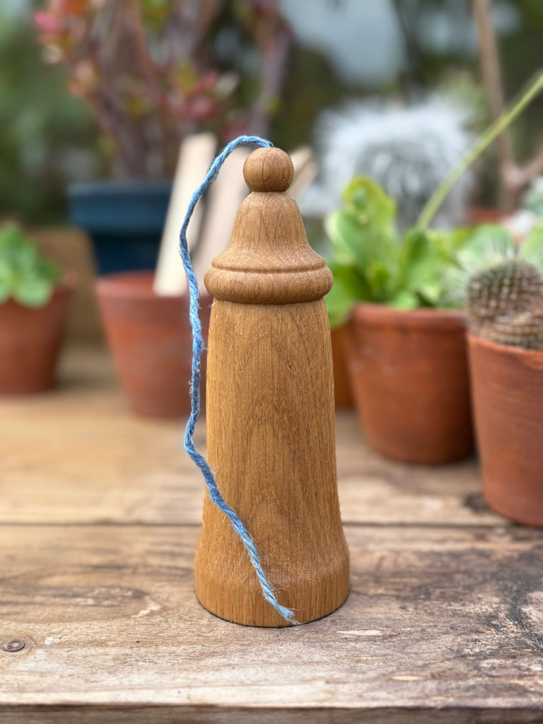 Wooden twine dispenser with blue jute twine on a wooden surface with plants in the background